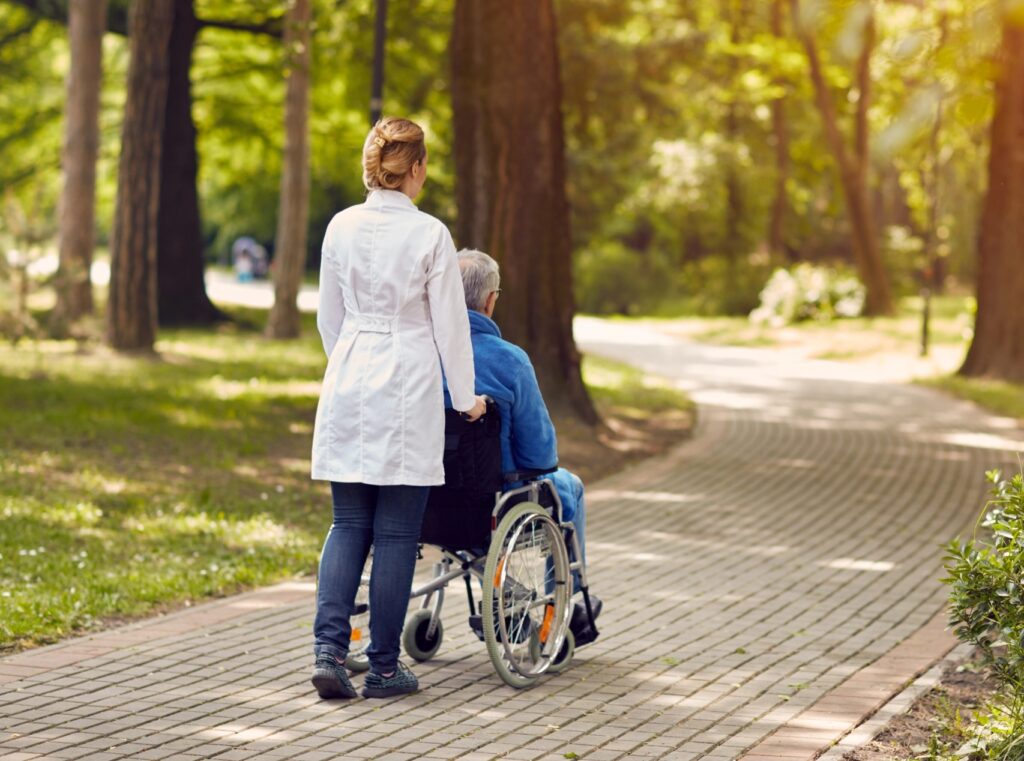 A woman in a white jacket pushing a man in a wheelchair down an outdoor pathway
