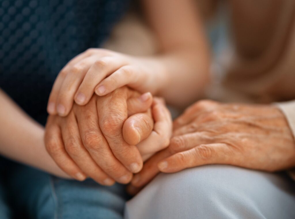 Close-up of a young person's hands intertwined with an older adult's hands