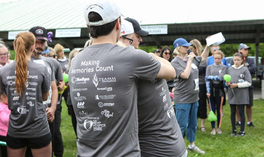 Two volunteers wearing KCN shirts hug in a crowd of other volunteers at a fundraising event
